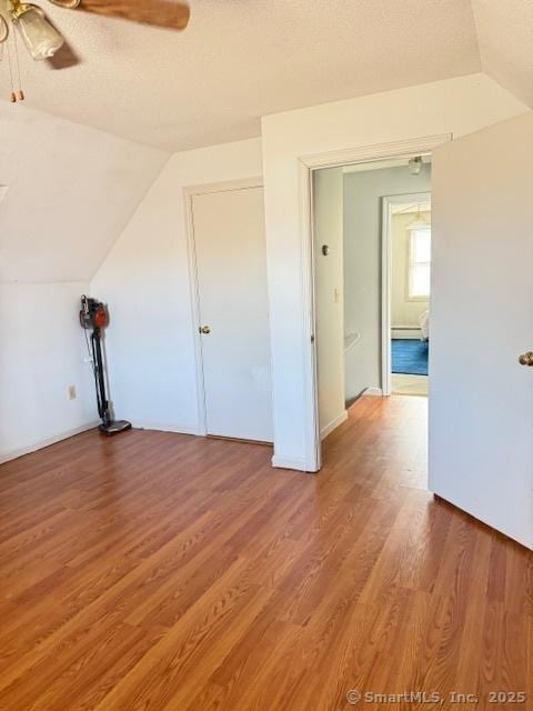 spare room with a textured ceiling, vaulted ceiling, wood finished floors, and ceiling fan