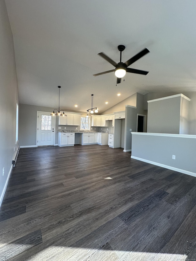 unfurnished living room with baseboards, ceiling fan with notable chandelier, dark wood finished floors, and vaulted ceiling