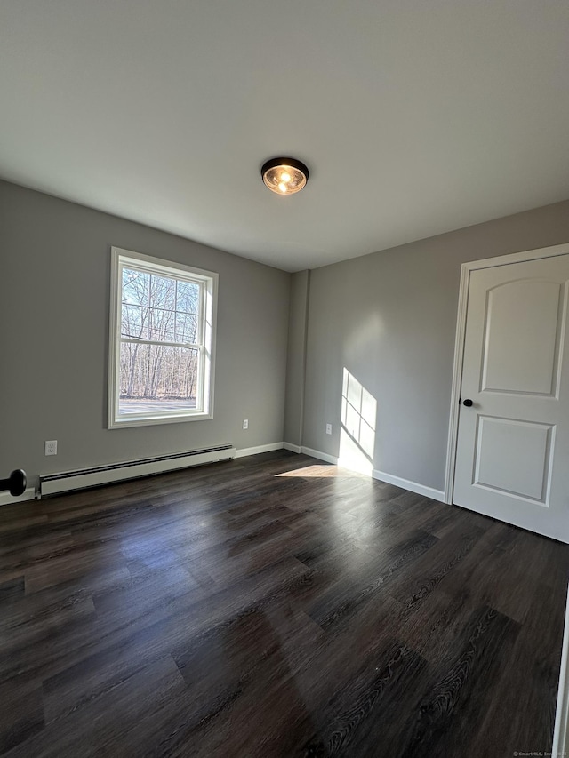 spare room featuring a baseboard heating unit, baseboards, and dark wood-style floors