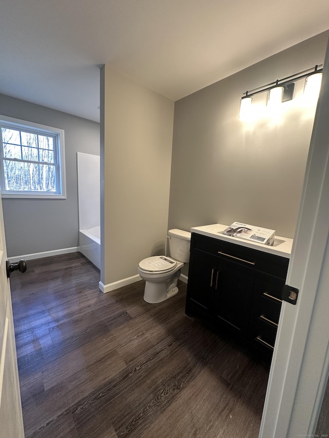 bathroom featuring toilet, wood finished floors, baseboards, a bath, and vanity