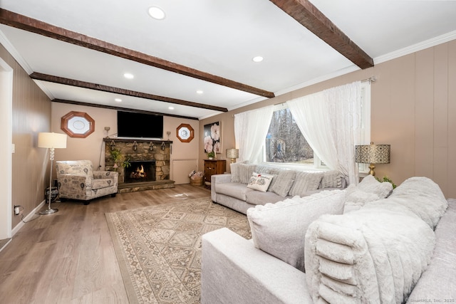 living room with beam ceiling, light wood-style floors, ornamental molding, and a fireplace