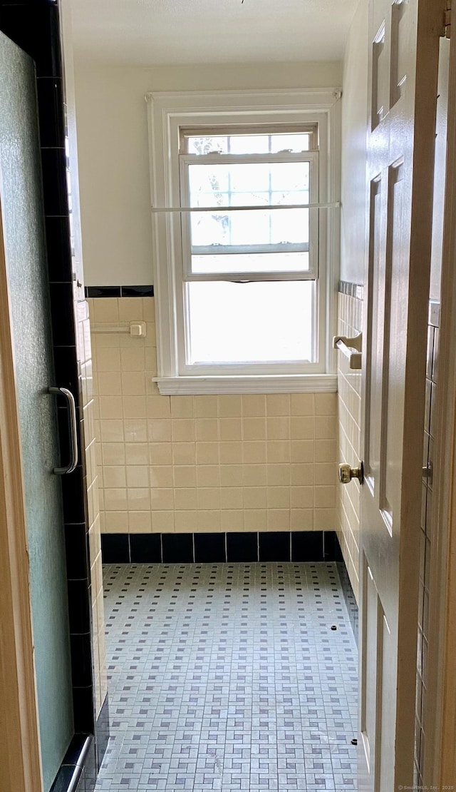 full bath featuring tile patterned flooring, tile walls, a wainscoted wall, and a shower stall