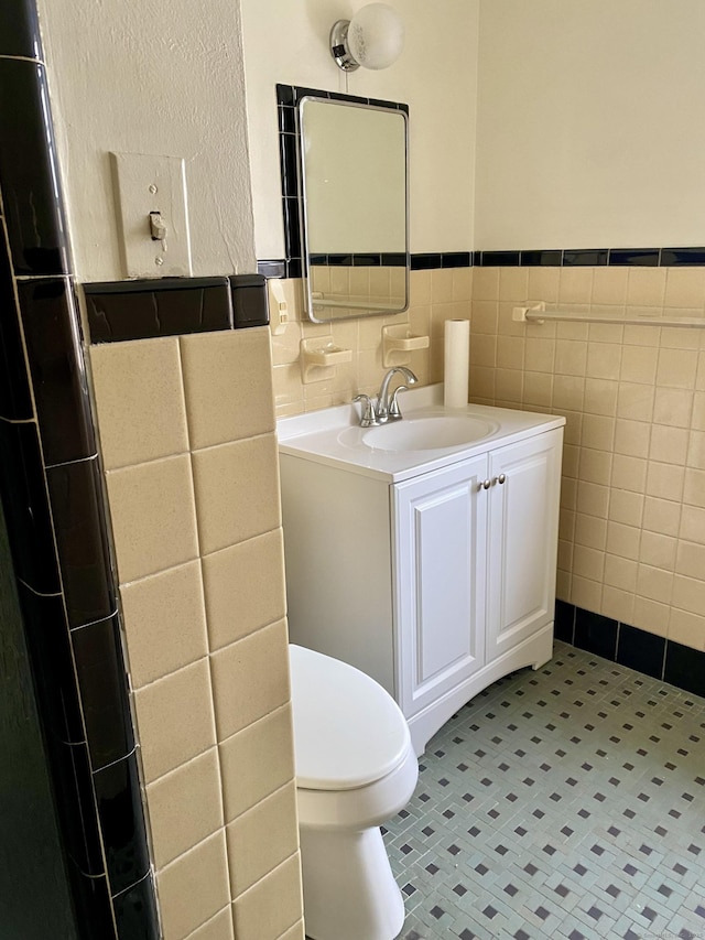 bathroom with wainscoting, vanity, toilet, and tile walls