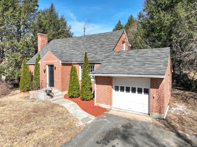 view of front of home featuring driveway, roof with shingles, a garage, brick siding, and a chimney