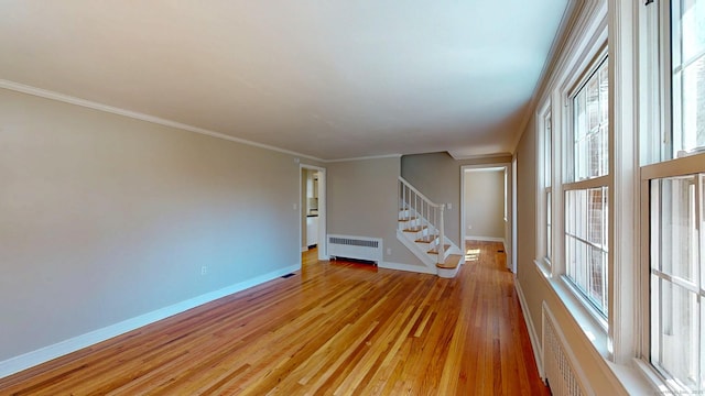 unfurnished room featuring light wood finished floors, radiator, crown molding, baseboards, and stairway