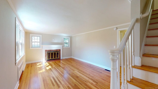 unfurnished living room featuring light wood finished floors, stairway, a brick fireplace, and crown molding