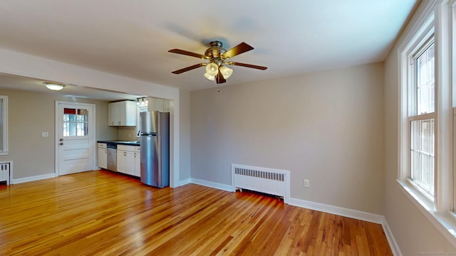 unfurnished living room with a ceiling fan, radiator heating unit, baseboards, and light wood-type flooring