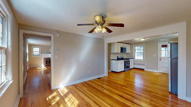 interior space with light wood finished floors, ceiling fan, radiator heating unit, appliances with stainless steel finishes, and white cabinetry