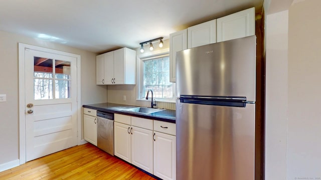 kitchen with light wood-style flooring, a sink, dark countertops, white cabinetry, and stainless steel appliances