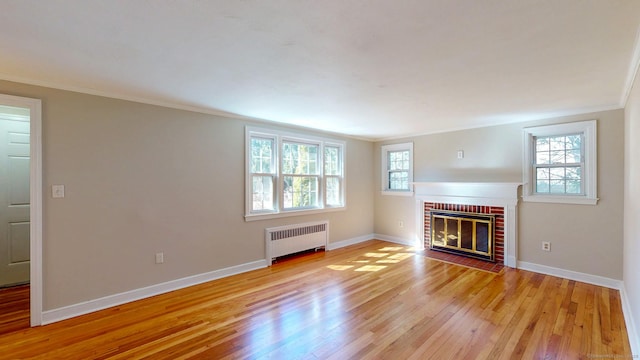 unfurnished living room with crown molding, radiator heating unit, light wood-style floors, and baseboards