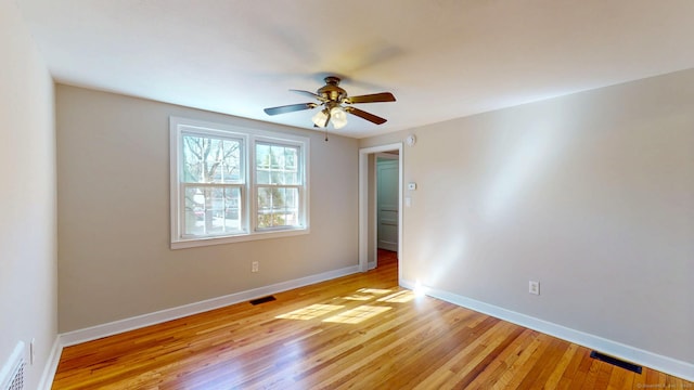 empty room with visible vents, light wood-style flooring, baseboards, and a ceiling fan