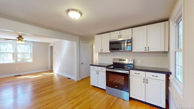 kitchen featuring white cabinetry, dark countertops, light wood-style floors, and stainless steel appliances