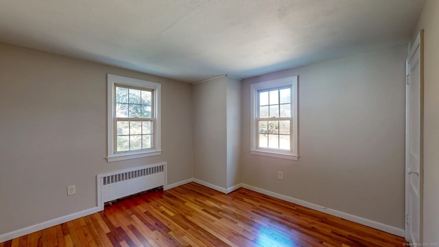 empty room featuring baseboards, radiator heating unit, and hardwood / wood-style flooring