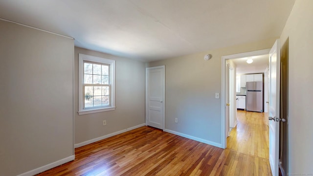 unfurnished bedroom with light wood-type flooring, baseboards, and freestanding refrigerator