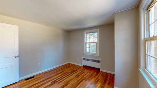 spare room with radiator, light wood-style floors, visible vents, and baseboards