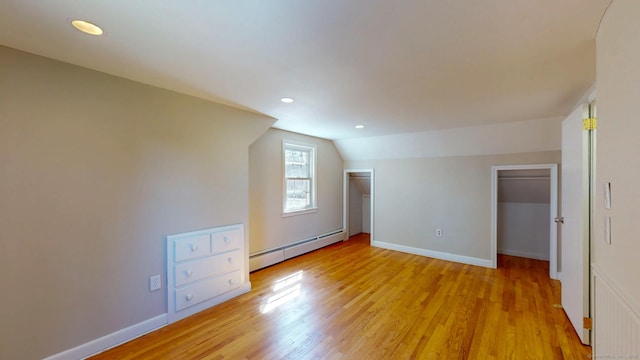 unfurnished bedroom featuring a baseboard radiator, baseboards, light wood-style flooring, and vaulted ceiling