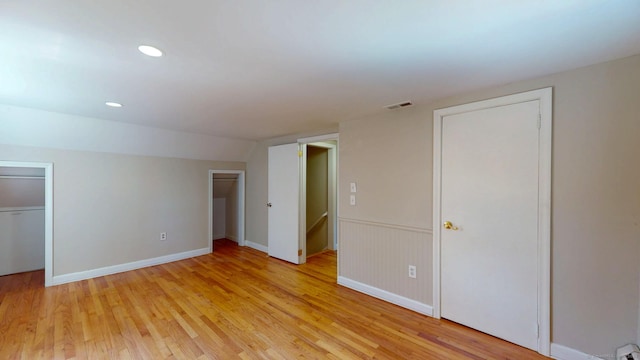 unfurnished bedroom featuring visible vents, recessed lighting, vaulted ceiling, multiple closets, and light wood-type flooring