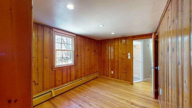 empty room with light wood finished floors, baseboard heating, recessed lighting, and wooden walls