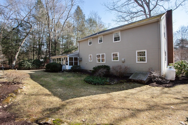 back of property featuring a lawn, a chimney, and a sunroom