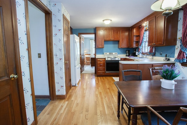 kitchen with electric stove, freestanding refrigerator, light wood-style floors, a peninsula, and light countertops