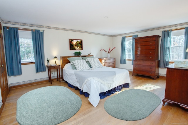 bedroom featuring a baseboard heating unit, crown molding, baseboards, and light wood-type flooring