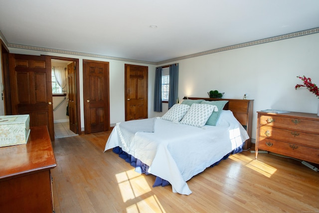 bedroom featuring light wood finished floors, two closets, baseboards, and ornamental molding