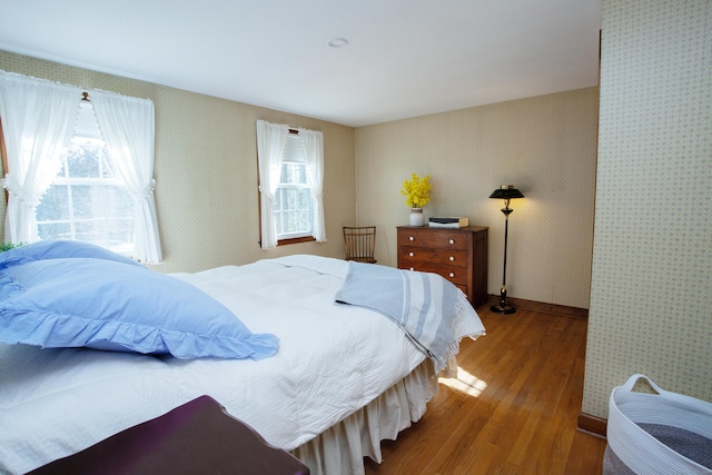 bedroom featuring baseboards, wood finished floors, and wallpapered walls