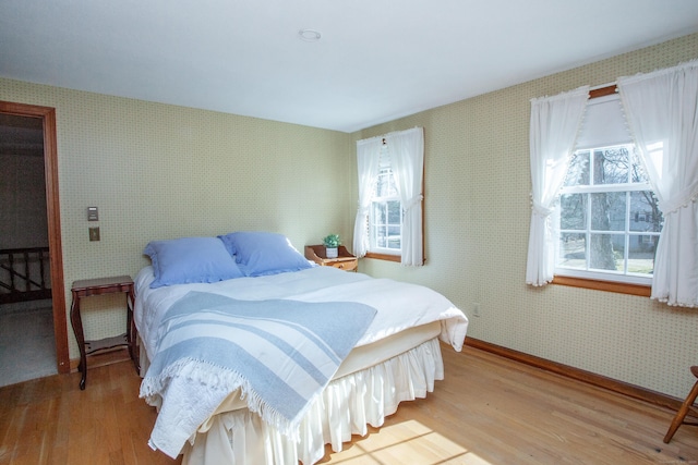 bedroom featuring wallpapered walls, wood finished floors, and baseboards