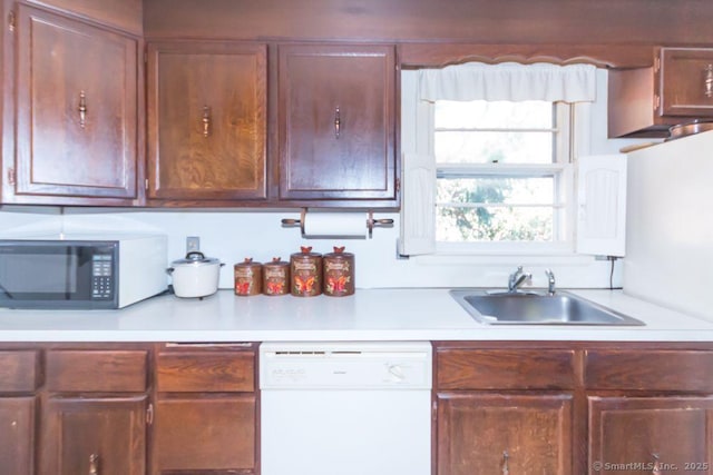 kitchen featuring a sink, light countertops, black microwave, and white dishwasher