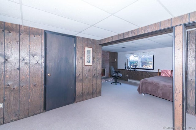 carpeted bedroom with a paneled ceiling and wood walls