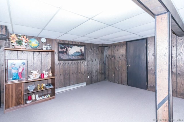 finished basement with wooden walls, carpet flooring, a baseboard heating unit, and a paneled ceiling