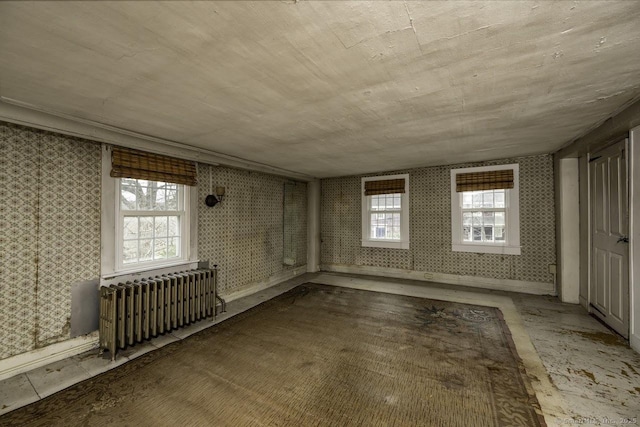 spare room with radiator, wallpapered walls, plenty of natural light, and baseboards