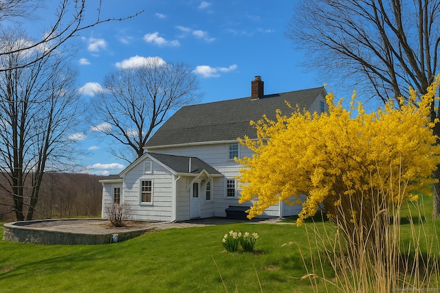 back of house featuring a lawn, a chimney, and a shingled roof