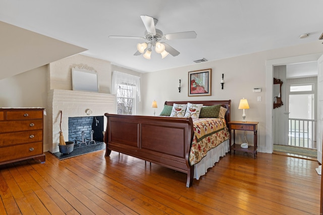 bedroom with visible vents, a brick fireplace, a ceiling fan, and hardwood / wood-style floors