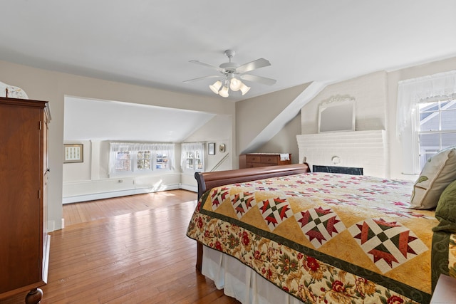 bedroom with a baseboard heating unit, lofted ceiling, a ceiling fan, and hardwood / wood-style flooring