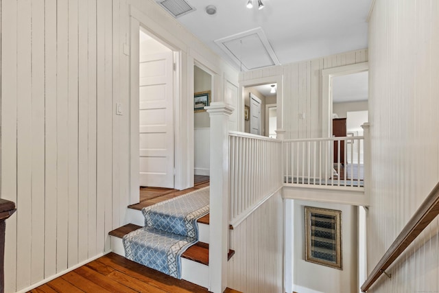 staircase with visible vents, wood walls, attic access, and wood finished floors