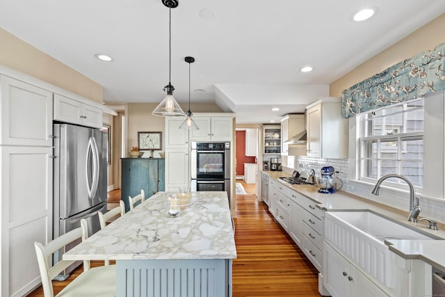 kitchen featuring a kitchen island, decorative backsplash, appliances with stainless steel finishes, wood finished floors, and a sink