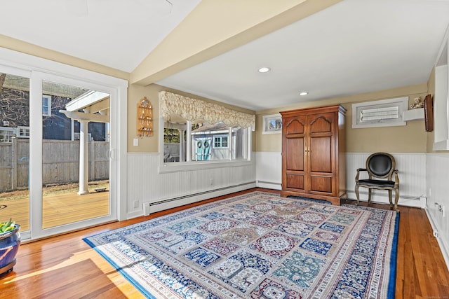 living area with a baseboard heating unit, lofted ceiling, wood finished floors, and wainscoting