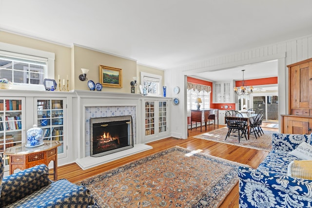 living area featuring a tiled fireplace, an inviting chandelier, wood finished floors, and a baseboard heating unit