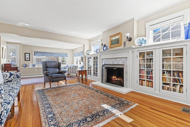 living area featuring a tiled fireplace, visible vents, wood finished floors, and a baseboard radiator