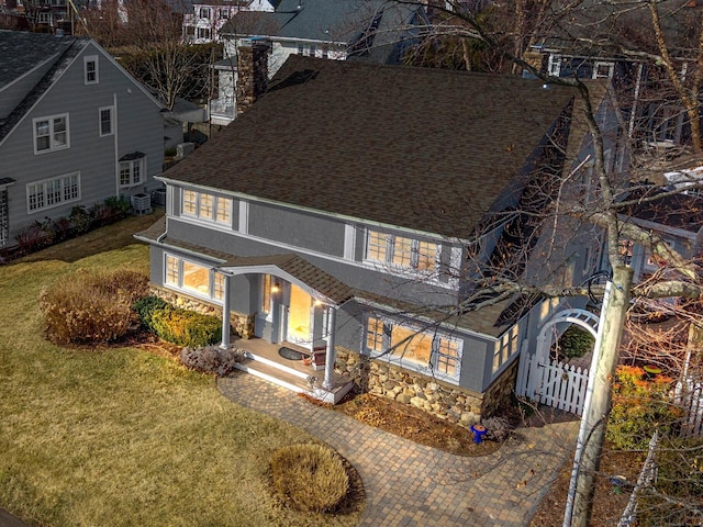 rear view of house with fence, central AC, a shingled roof, stone siding, and a lawn