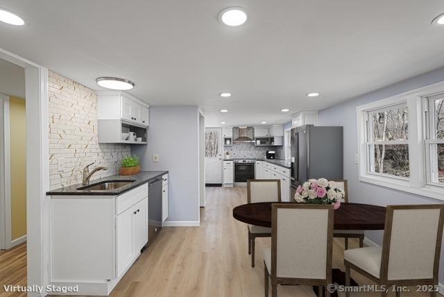 129 Smith Rd, East Haddam, CT 06423 - kitchen featuring wall chimney range hood, a sink, stainless steel appliances, backsplash, and white cabinetry