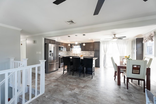 dining room with ornamental molding, light wood-style floors, visible vents, and ceiling fan