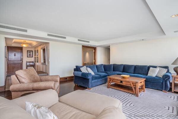 living area with a tray ceiling, wood finished floors, and visible vents