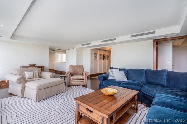 living area with visible vents, a raised ceiling, and wood finished floors