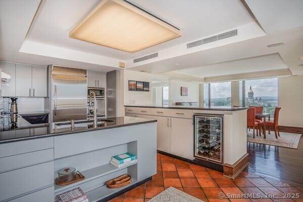 kitchen with a tray ceiling, built in refrigerator, visible vents, and beverage cooler