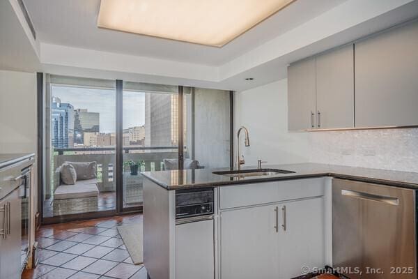 kitchen with a sink, stainless steel dishwasher, a peninsula, light tile patterned flooring, and a raised ceiling