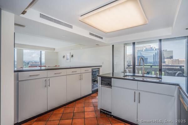 kitchen featuring beverage cooler, visible vents, dark tile patterned flooring, a sink, and white cabinets