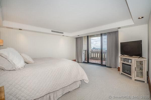 carpeted bedroom with visible vents, a tray ceiling, and access to outside