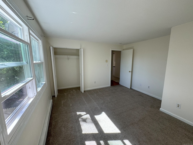 unfurnished bedroom with a closet, baseboard heating, baseboards, and carpet